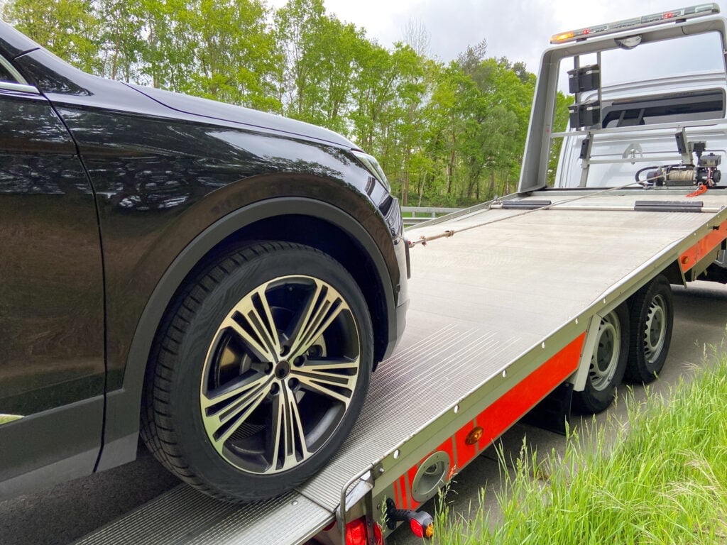 Black car being loaded onto a red and gray flatbed tow truck on a highway, trees in background